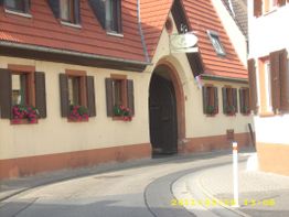 Eine Straße mit einem Fachwerkhaus, blumengeschmückte Fenster und ein Torbogen im Vordergrund.