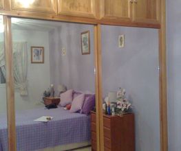 Armario con espejo en habitación de paredes lilas, cama con sábanas moradas y mesa de noche.