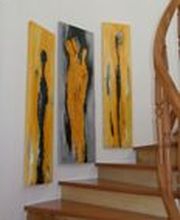 Drei abstrakte Gemälde in Gelb und Schwarz hängen an einer Wand neben einer Holztreppe.