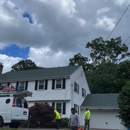 Workers in front of a two-story house on a cloudy day, with a van parked in the driveway.