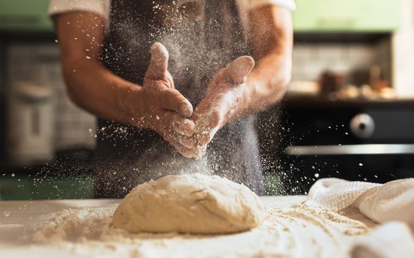 Ein Bäcker bestäubt den Teig eines Sauerteigbrots mit Mehl.
