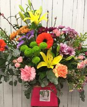 Ramo de flores coloridas con lilas, gerberas, y lirios amarillos sobre fondo de madera clara.