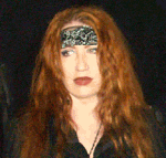 Frau mit roten Haaren und schwarzem Stirnband vor dunklem Hintergrund.