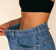 Person mit schwarzem Top zeigt lockere Jeans am Bauch, symbolisierend Gewichtsverlust.