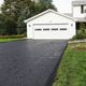 Newly paved driveway leading to a white garage attached to a house with a green lawn.