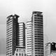 Drei moderne Hochhäuser vor bewölktem Himmel, in Schwarzweißaufnahme.