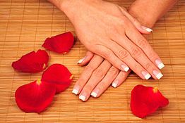 Hände mit französischer Maniküre auf Bambusmatte, umgeben von roten Rosenblättern.