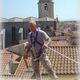 Man in a safety harness working on a rooftop in a historic city setting.