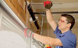 Man wearing gloves and goggles repairing a garage door mechanism.
