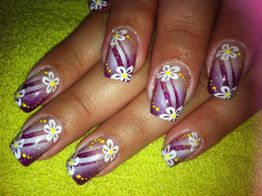Nägel mit lila Glitzer und weißen Blumen auf grünem Hintergrund.