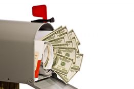 Mailbox with red flag open, stuffed with envelopes and US dollar bills protruding.