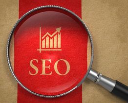 Magnifying glass over "SEO" text with upward graph on red background.