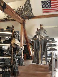 Ein Raum mit Militärkleidung und Ausrüstung, US-Flagge, Tarnnetz hängt an der Decke.