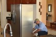 Person fixing a stainless steel refrigerator in a kitchen setting.