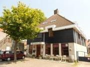 Een hoekgebouw met zwart-witte gevel en een terras onder een boom.