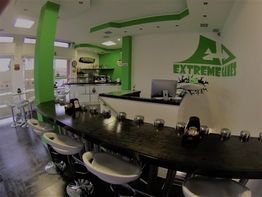 Interno di un bar moderno con tema verde e nero, bancone curvo e sedie bianche.