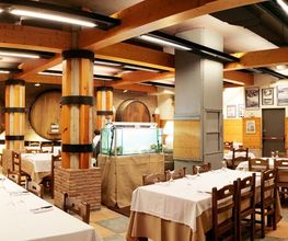 Restaurante rústico con mesas blancas y barriles grandes de madera en las paredes.