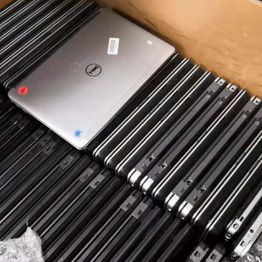 Several laptops stacked, mostly black, one silver Dell on top, in a cardboard box.