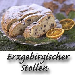 Erzgebirgischer Stollen auf einem Teller, umgeben von Tannenzweigen und getrockneten Orangenscheiben.