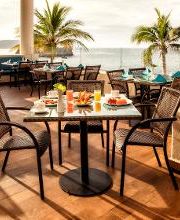 Mesa con desayuno junto al mar en terraza con palmeras.