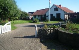 Einfamilienhaus mit Garten, gepflasterter Weg, Steinmauer, Fahne und weißem Holztor.