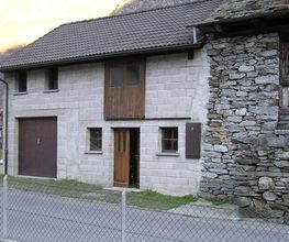 Steinhaus mit Holzelementen, zweistöckig, Zaun im Vordergrund, Berglandschaft im Hintergrund.