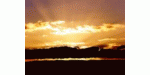 Sonnenuntergang über einem See mit reflektierendem Wasser und Wolken am Himmel.