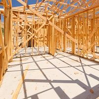 Wooden framing of a house under construction, with clear blue sky background.