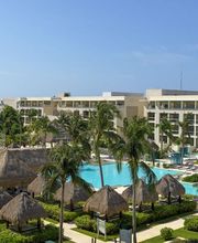 Complejo turístico con piscinas, palapas y palmeras bajo un cielo azul despejado.