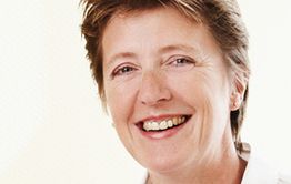 Eine lächelnde Frau mit kurzen Haaren vor einem hellen Hintergrund.