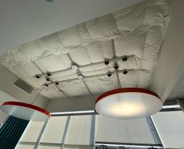Ceiling view with insulated panels and two large circular hanging lights, daylight through windows.