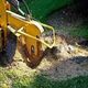 Yellow stump grinder in action, removing a tree stump on a grassy lawn.