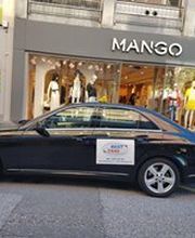 Schwarzes Auto vor einem Mango-Geschäft geparkt. Links ein Schild.