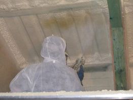 Person im Schutzanzug sprüht Isolierung an Decke.