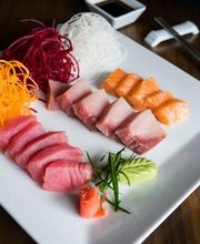 Plato de sashimi con salmón y atún, acompañado de vegetales en tiras y wasabi.