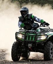 Persona manejando un cuatriciclo verde en un camino de tierra, levantando polvo a su alrededor.