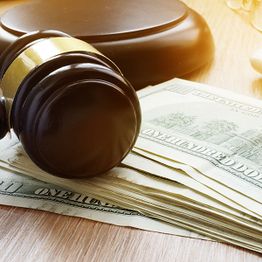 Gavel resting on a stack of hundred-dollar bills on a wooden table.