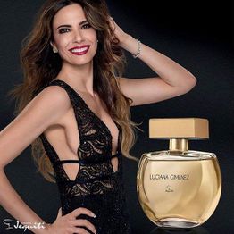 Mulher sorrindo em vestido preto ao lado de perfume com rótulo "Luciana Gimenez, Jequiti".