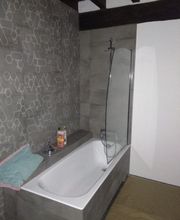 Baño moderno con bañera, toalla doblada, y productos en el borde. Pared con diseño geométrico.