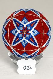 Rote Temari-Kugel mit blauen Mustern auf einem Glasständer, beschriftet mit "024".