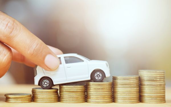 Stapel mit Geldmünzen über die ein Spielzeugauto fährt