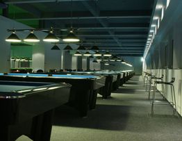 Reihe von Billardtischen in einem Raum mit Hängelampen, leeren Stühlen und gedämpfter Beleuchtung.