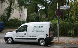 Ein weißer Lieferwagen mit "ONKEL TOM" steht an der Onkel-Tom-Straße, umgeben von Bäumen.
