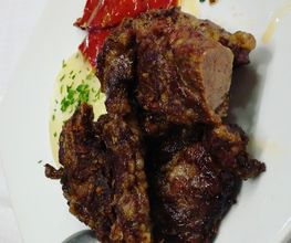 Plato de carne asada con guarnición de pimientos rojos y salsa en un plato blanco.
