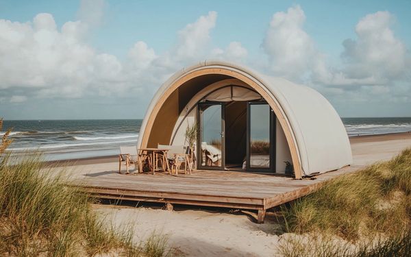 Ein luxuriöses Zelt am Strand zwischen Dünen, bei bewölktem Himmel und stürmischen Meer.