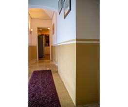 Flur mit beigem Anstrich, lila Teppichläufer und schmalen Streifen entlang der Wand.