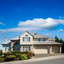 Two-story suburban house with a driveway, surrounded by greenery and a clear blue sky.