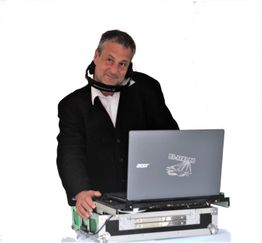 Ein Mann mit Headset steht an einem DJ-Pult mit Laptop und Mischpult.