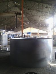 Tanque metálico grande en un almacén industrial con techo alto y maquinaria alrededor.