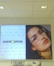 Poster aan de muur van een opticien met merklogo en een vrouw die een bril draagt.